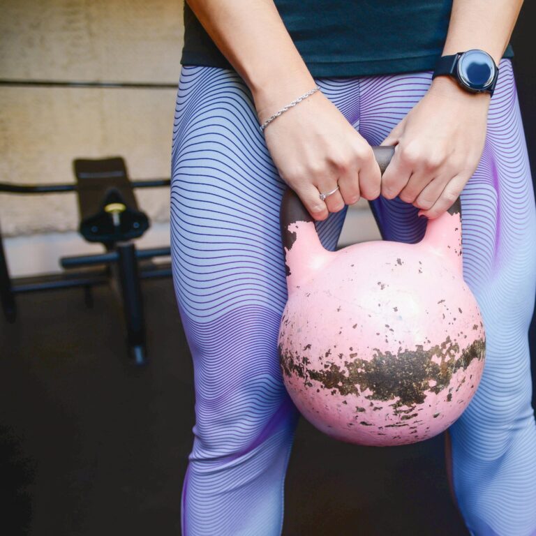 Fit woman holding a pink kettlebell during a workout session indoors.